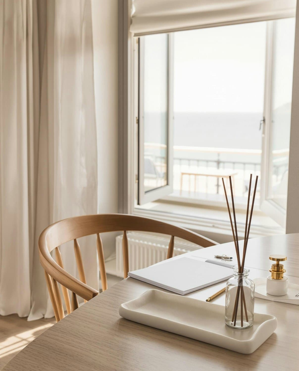 A quiet desk with a notebook and a wooden chair by an open window overlooking the sea
